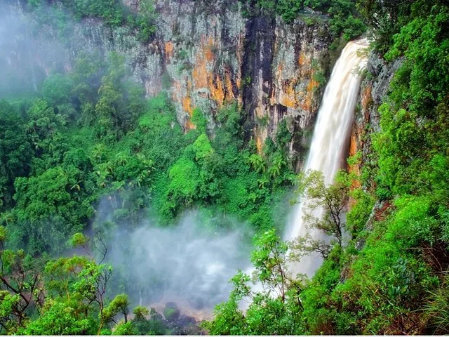 A scenic view of a tall waterfall surrounded by lush green forest.