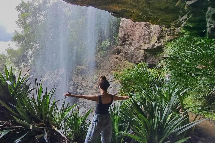 Woman standing with arms outstretched behind a cascading waterfall in a lush forest