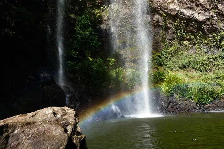 A waterfall pouring into a pool, creating a bright rainbow above the water