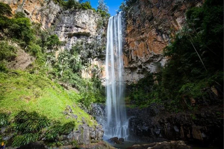 Tall, powerful waterfall plunging down a sheer rocky cliff surrounded by lush vegetation.