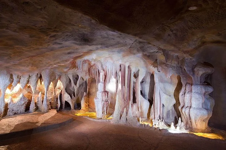 An illuminated cave features stalactites and stalagmites along a smooth walking path.