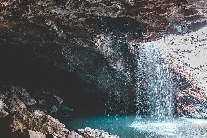Water cascades down from a rocky cave overhang into a blue pool below.